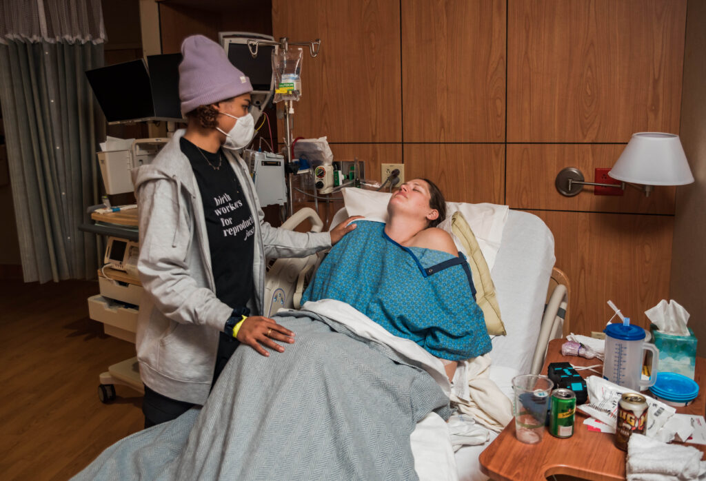 Doula supporting laboring mother in a hospital bed. UC Health Anschutz hospital birth photography.