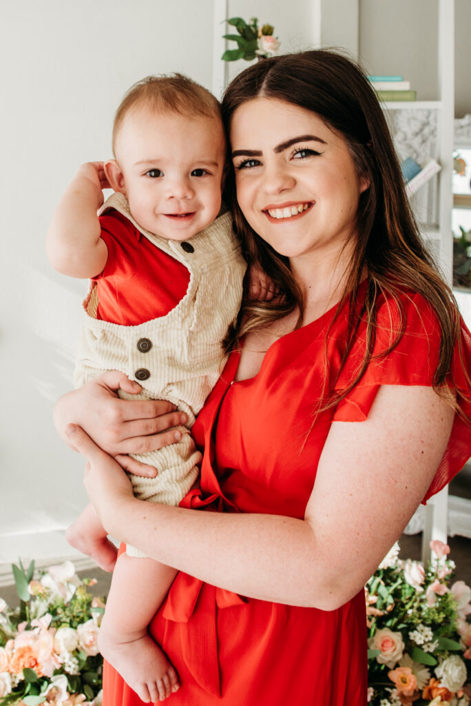 Floral studio mother's day mini sessions mom in red dress with son in arms.