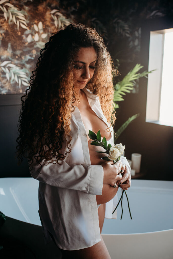 Studio pregnancy photography in Northern Colorado. White shirt, bare belly, tub, and flowers.