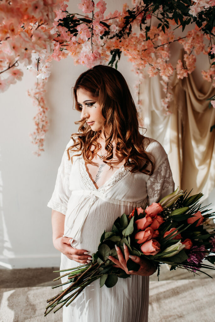 Studio maternity photography in Longmont Colorado. Pink flowers, white dress.