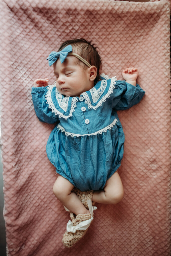 Baby girl sleeping in blue dress with white lace on a pink blanket
