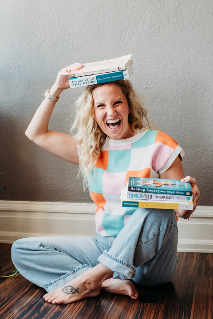 Motherhood Untamed IBCLC lactation support, breastfeeding help. Woman holding breastfeeding related books in her lap and on her head.