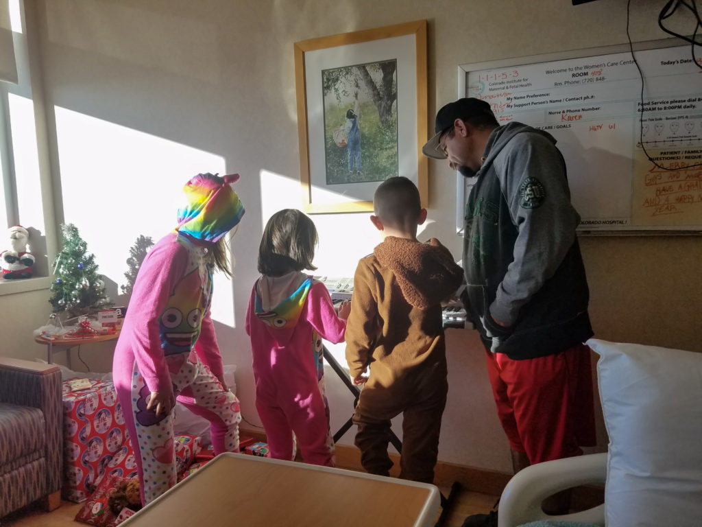 Kids looking at their new gifts while celebrating Christmas morning in the hospital with their pregnant mom