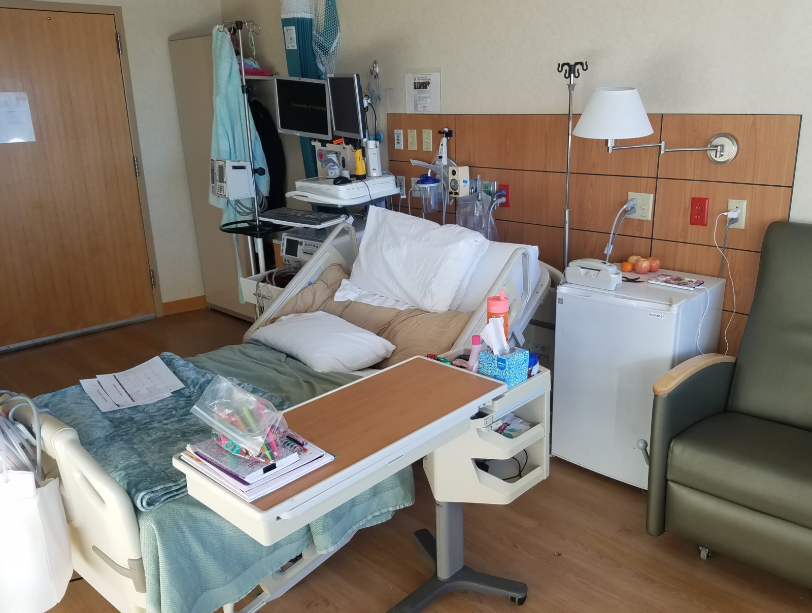 A photo of the hospital room the author spent over two weeks in at UCHealth Anschutz in Aurora Colorado. Shows authors own belongings amongst the hospital equipment.
