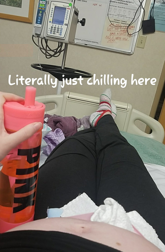 The pregnant author laying in a hospital bed with a large water bottle. It reads "literally just chilling here." 