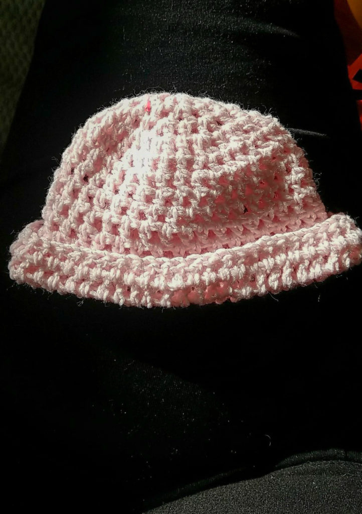 A tiny pink crochet hat that the author made while on hospitalized bed rest