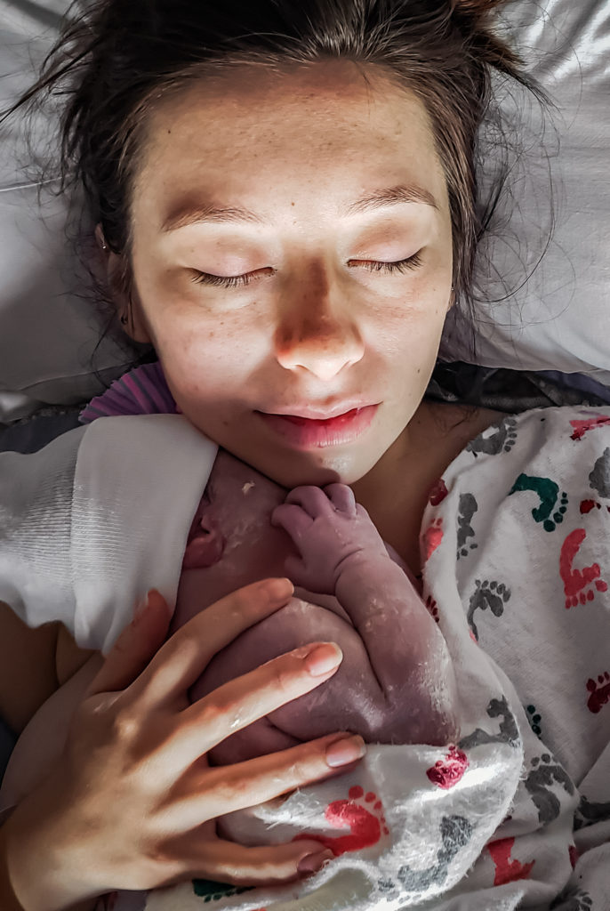 Woman with closed eyes holds her brand new baby close and breathes her first moments in.