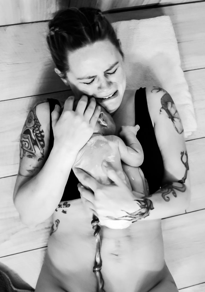 Mama holding her baby for the first time after giving birth on the floor of her bathroom at home. home birth frederick colorado birth photography. 