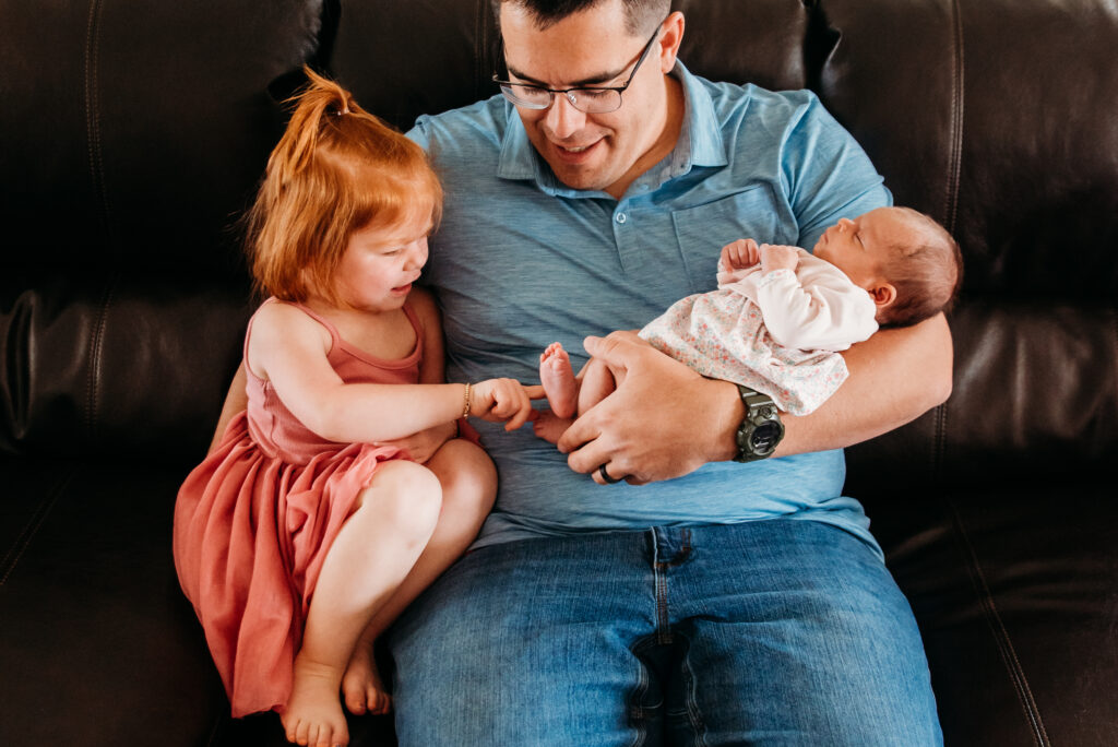 Photo of big sister touching baby sister's foot by Longmont Colorado newborn photographer
