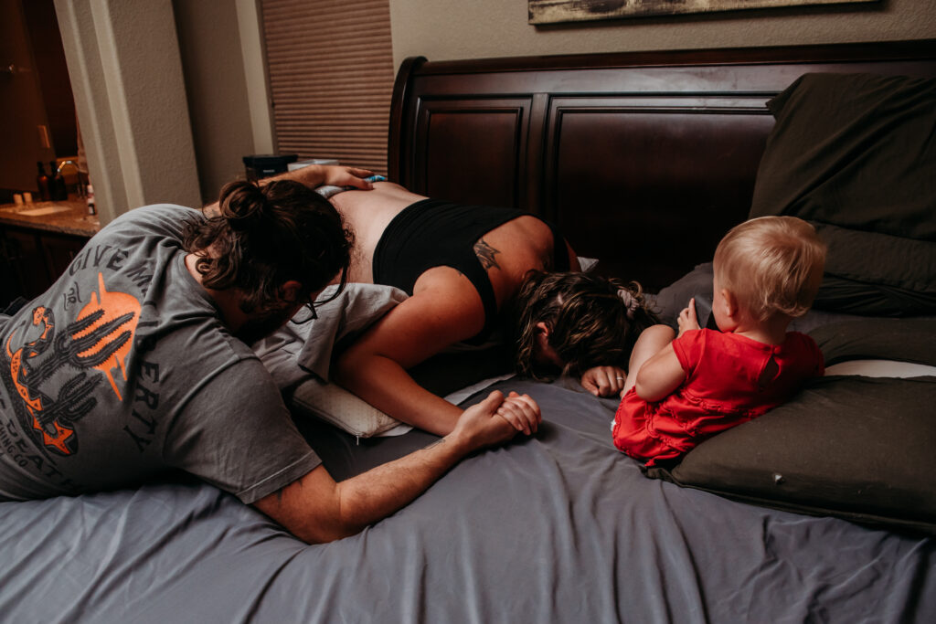 Mom laboring on her bed with her husband and 2 year old daughter by her side. 