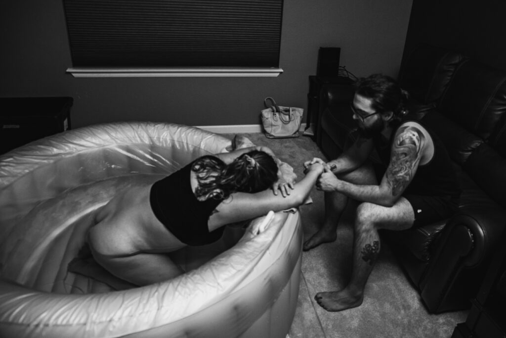 Laboring woman in a white birth tub holding on to husband's hand.
