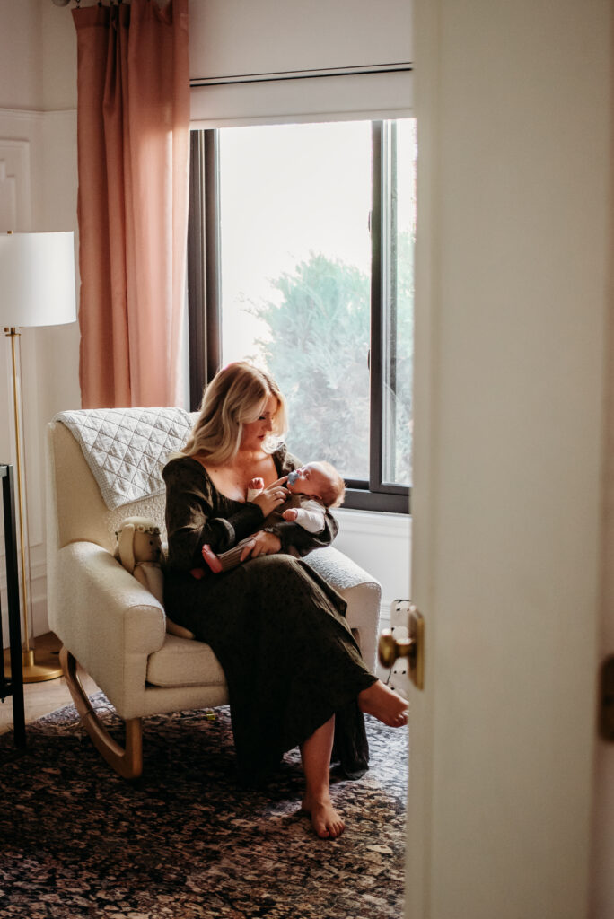 Mom holding new baby in rocker in baby's nursery in their home newborn photo session