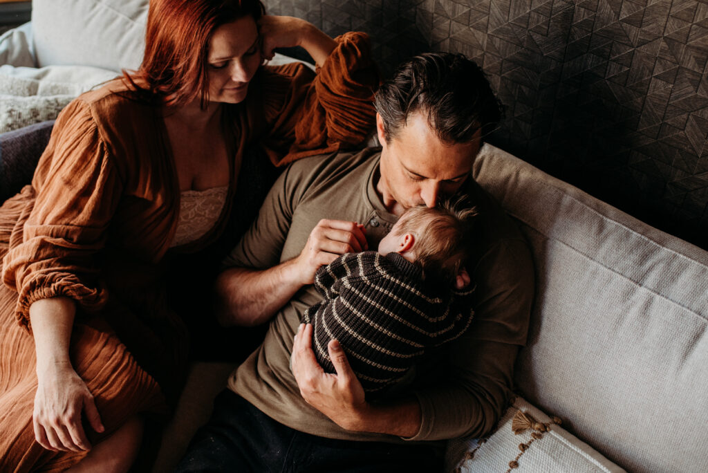 Mom and dad cuddling new baby on their couch during their lifestyle newborn photo session
