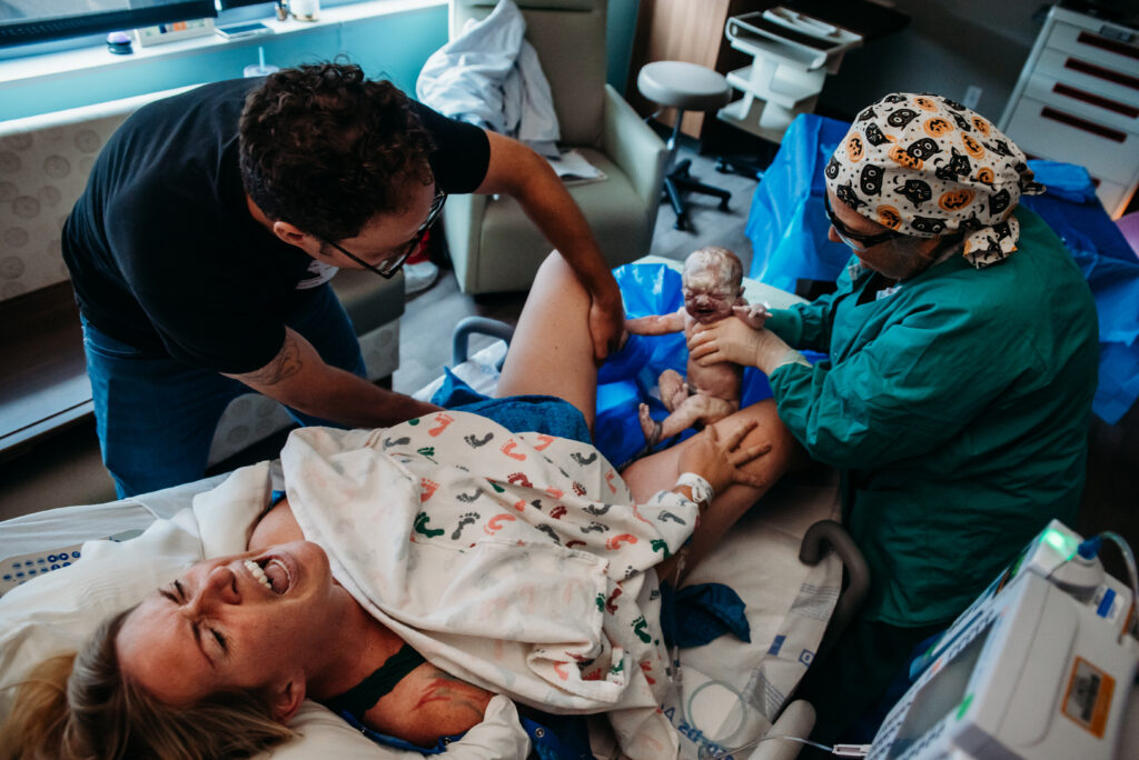 Mom roaring as baby emerges and is birthed. Dad holding mom's leg, doctor catching baby at Longs Peak Hospital in Longmont Colorado