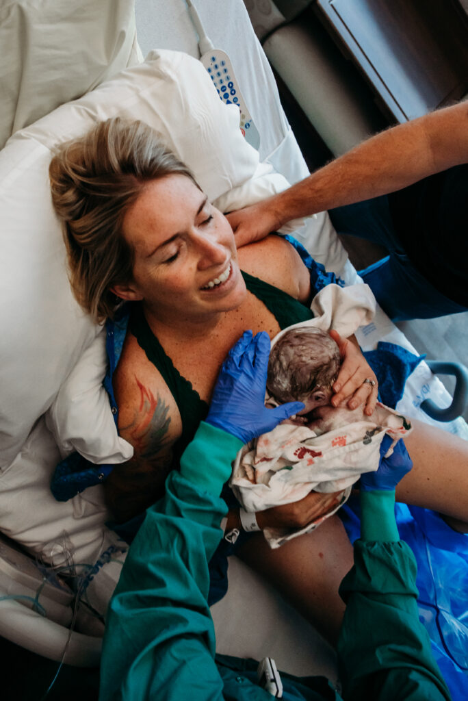 Mom holding her just born baby against her chest for the first time with a look of I did it on her face and a smile. Longs Peak Hospital Firestone Colorado