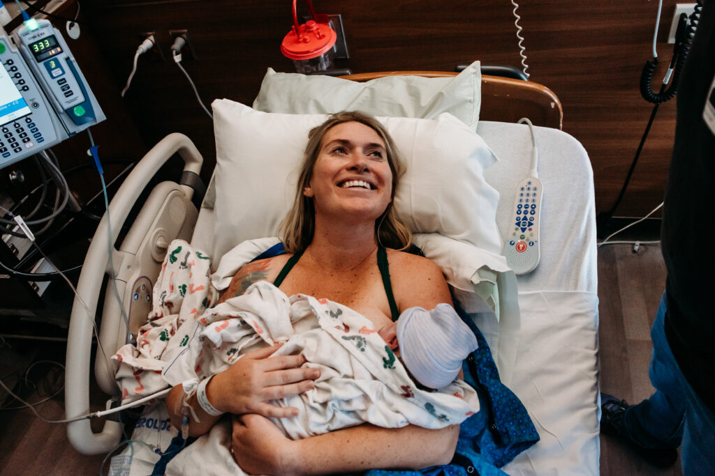 Mom smiling and holding just born baby girl for the first time. Photo of a surprise gender birth story in Longmont Colorado