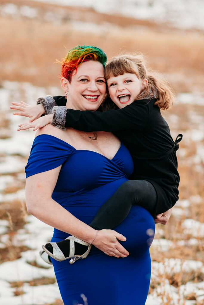 Pregnant mom holding daughter wearing royal blue maternity dress.