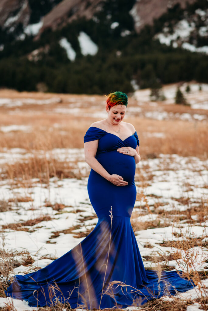 Pregnant mom with rainbow hair in blue dress in front of the Boulder CO flatirons.