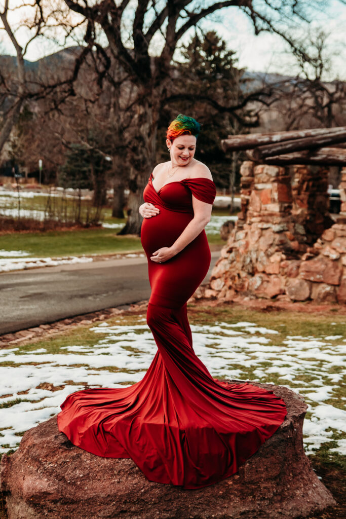 Pregnant mom embracing her belly wearing a red maternity dress at Chautauqua in Boulder CO