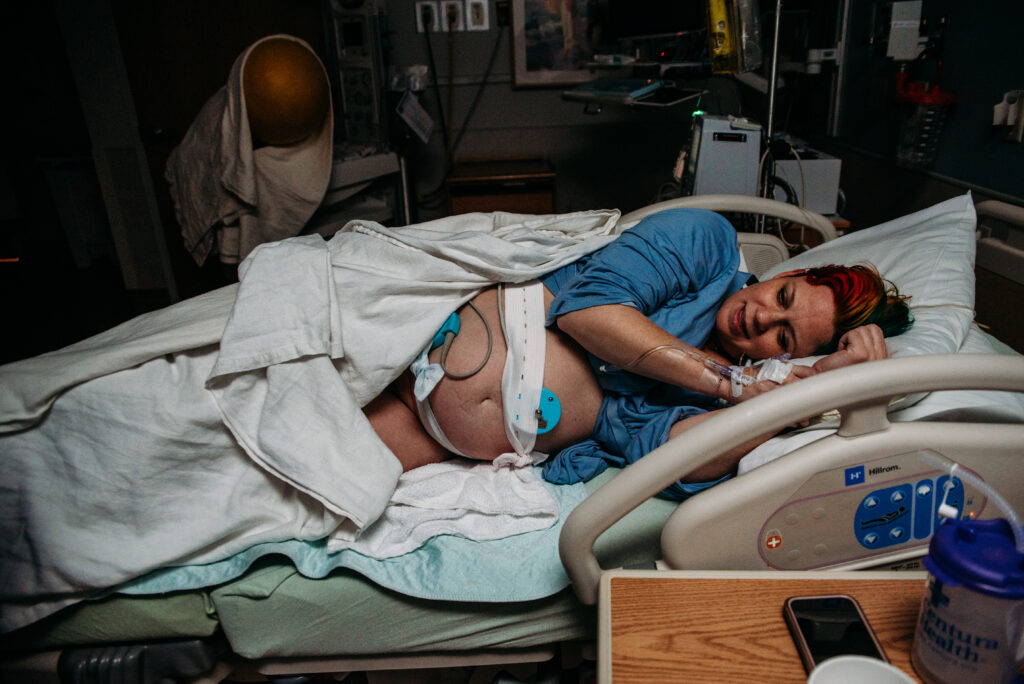 Pregnant mom laying in a hospital bed in Longmont CO with monitors attached to her belly, laboring to meet her baby.