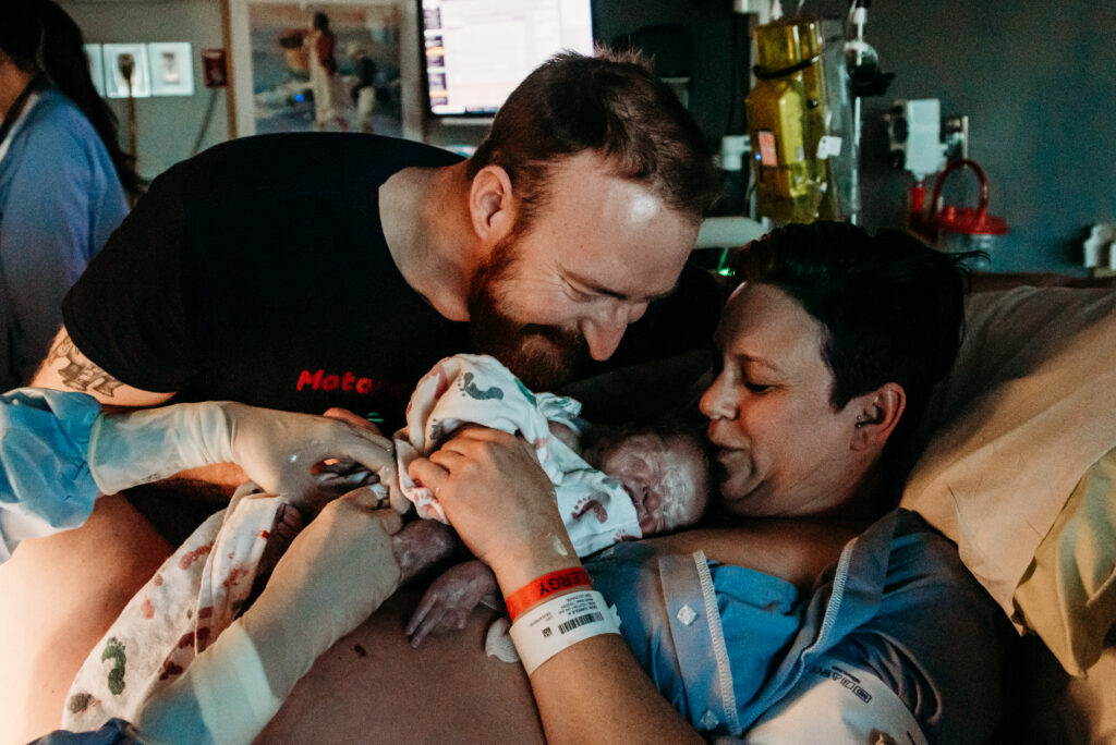 Mom and  dad kissing and admiring their just born baby boy in the hospital bed in Longmont Colorado