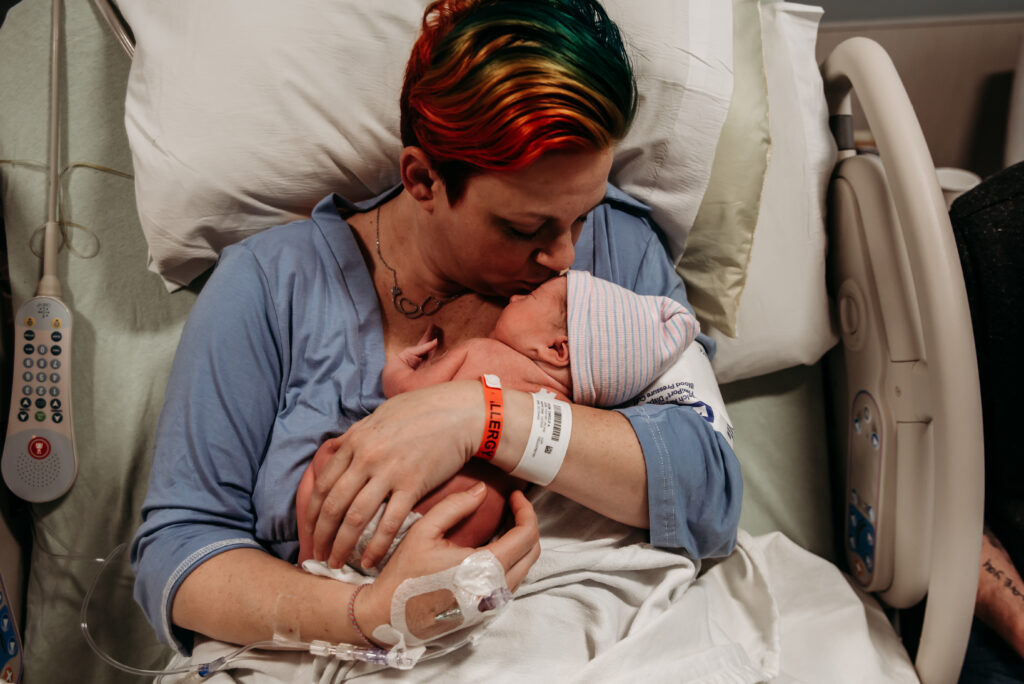 Mom in hospital bed at Longmont United Hospital holding and kissing her brand new baby