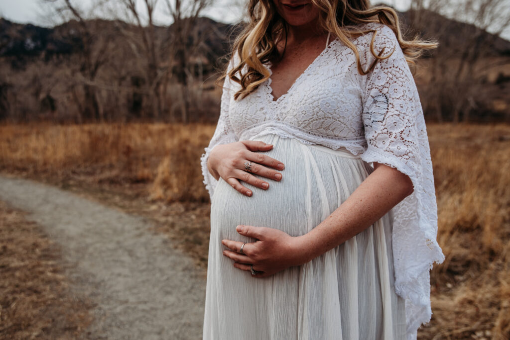 Close up photo of pregnant belly whearing white dress with long flowy sleeves in Boulder CO