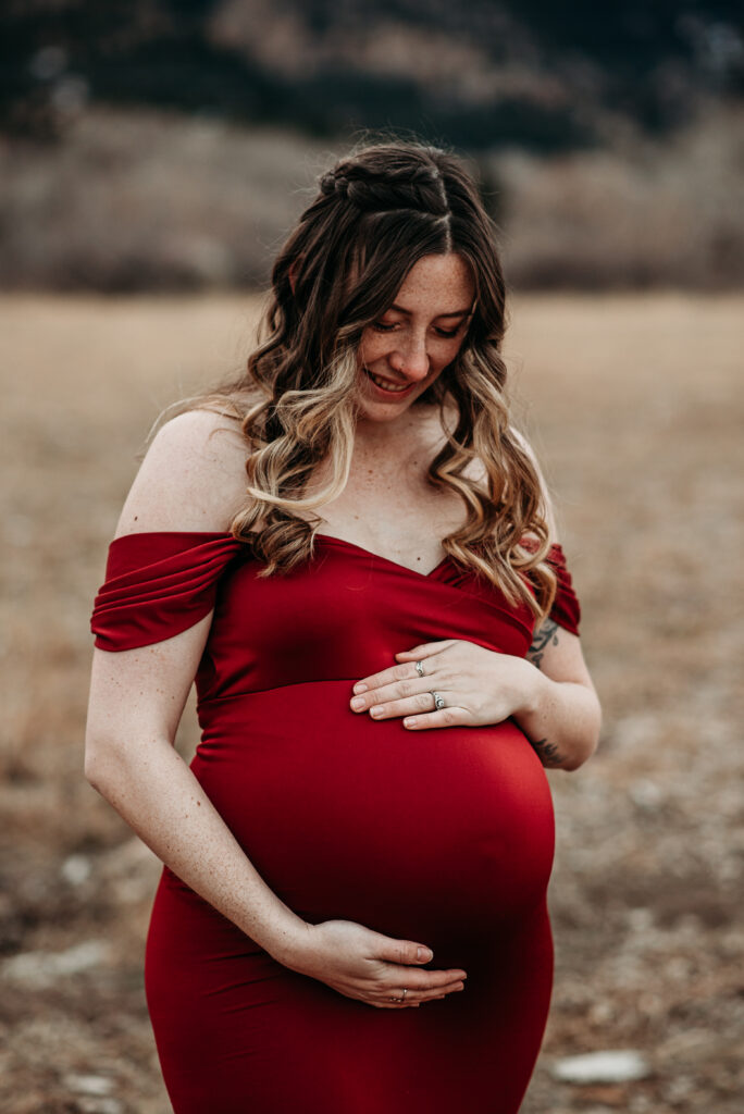 Embracing belly in red maternity dress in Boulder CO