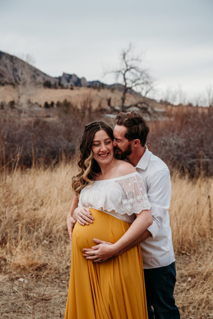 Dad snuggling pregnant mom in yellow maternity dress with white top in Boulder county CO