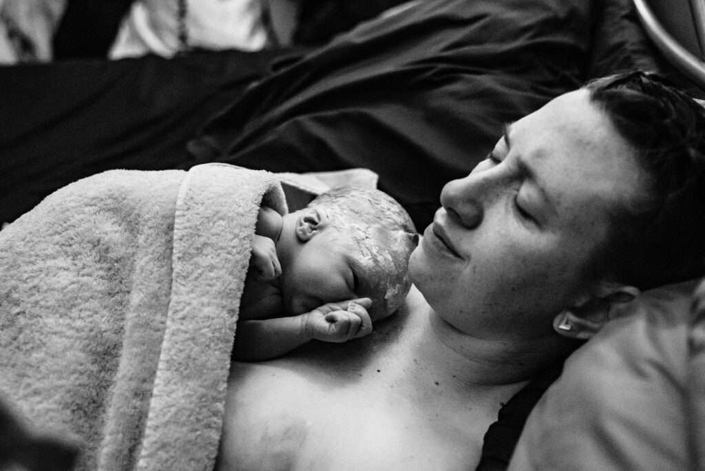 Mom takes a moment to close her eyes and breathe while holding her just born baby boy skin to skin against her chest on the bed at Seasons community birth center