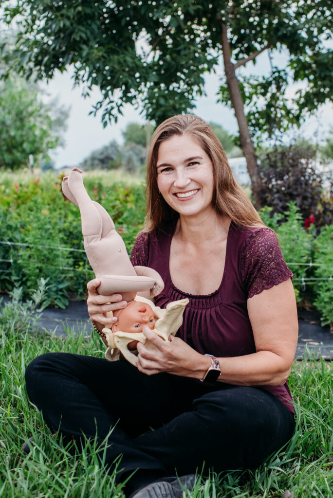 Northern CO home birth midwife sitting with a baby doll motioning through a  model of a pelvis in her hands.