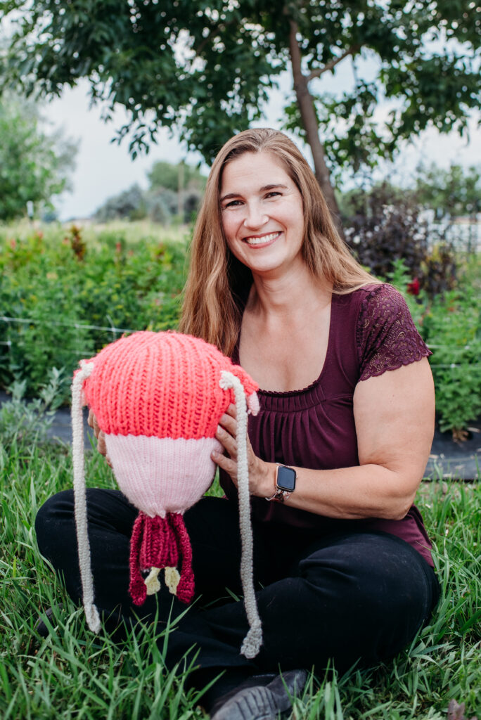 Northern CO home birth midwife sitting with a crotcheted uterus with dangling fallopian tubes in her hands