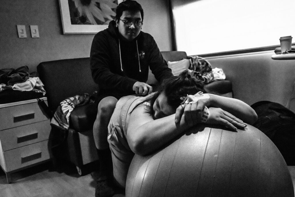 Dad supporting laboring mom leaning on a yoga ball. Labor and birth photography at Children's Hospital Colorado