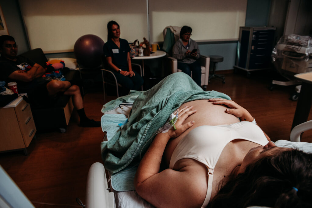 Mom holding pregnant belly in hospital bed with family surrounding her at Children's Hospital Colorado