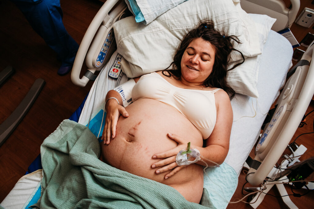 Mom smiling and holding belly in hospital bed at Children's Hospital Anschutz