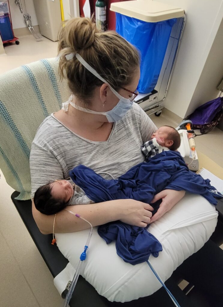 Holding both of my twins in the NICU connected to two different machines wearing a mask.