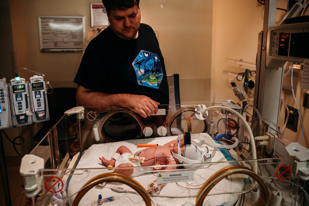 UCHealth Anschutz NICU birth stories - Dad looking at new baby girl in isolette.