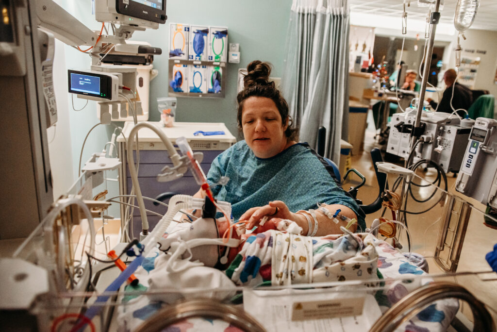 UCHealth Anschutz NICU birth stories - Mom looking at new baby girl in isolette.