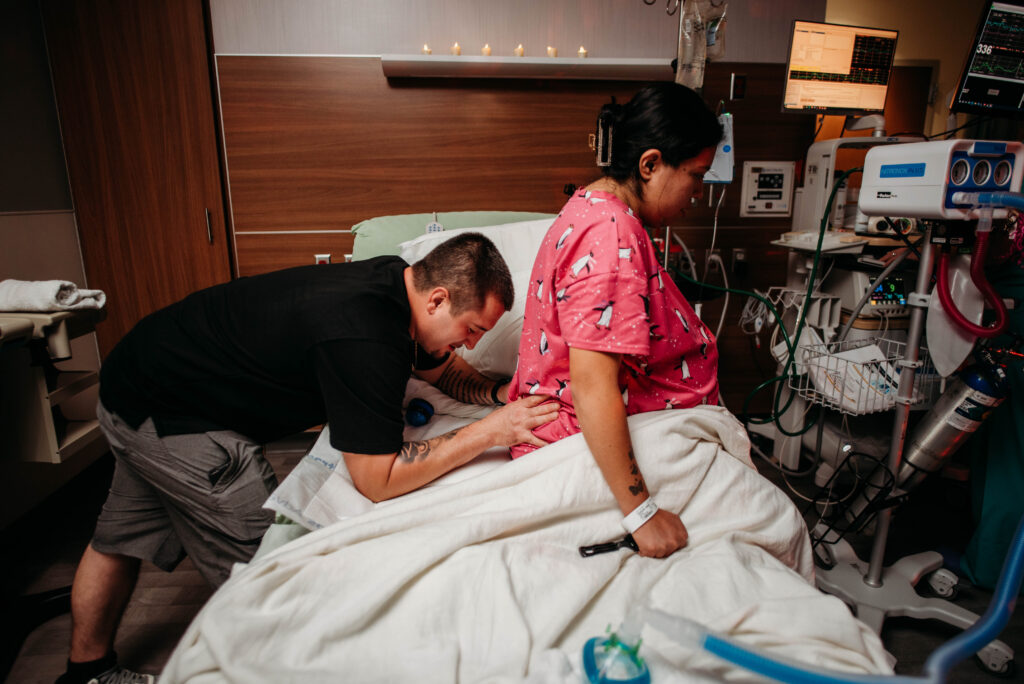 Birth photo of husband rubbing laboring mom's back during labor at Longs Peak Hospital in Longmont CO