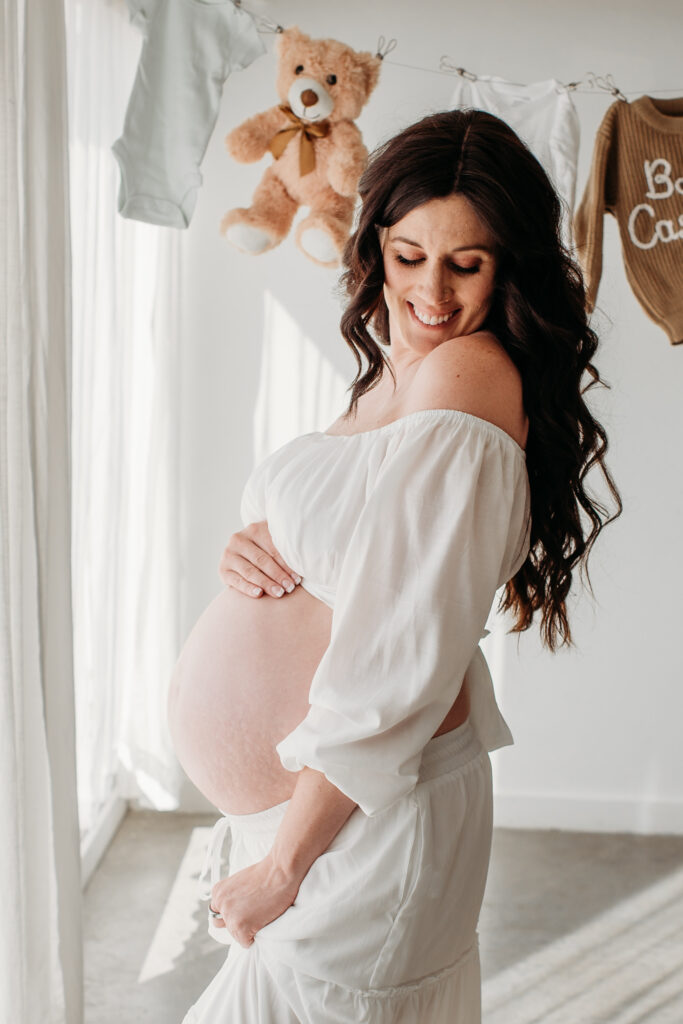 Pregnant mama wearing two piece white dress with belly out. Sugarhill Photo Studio.