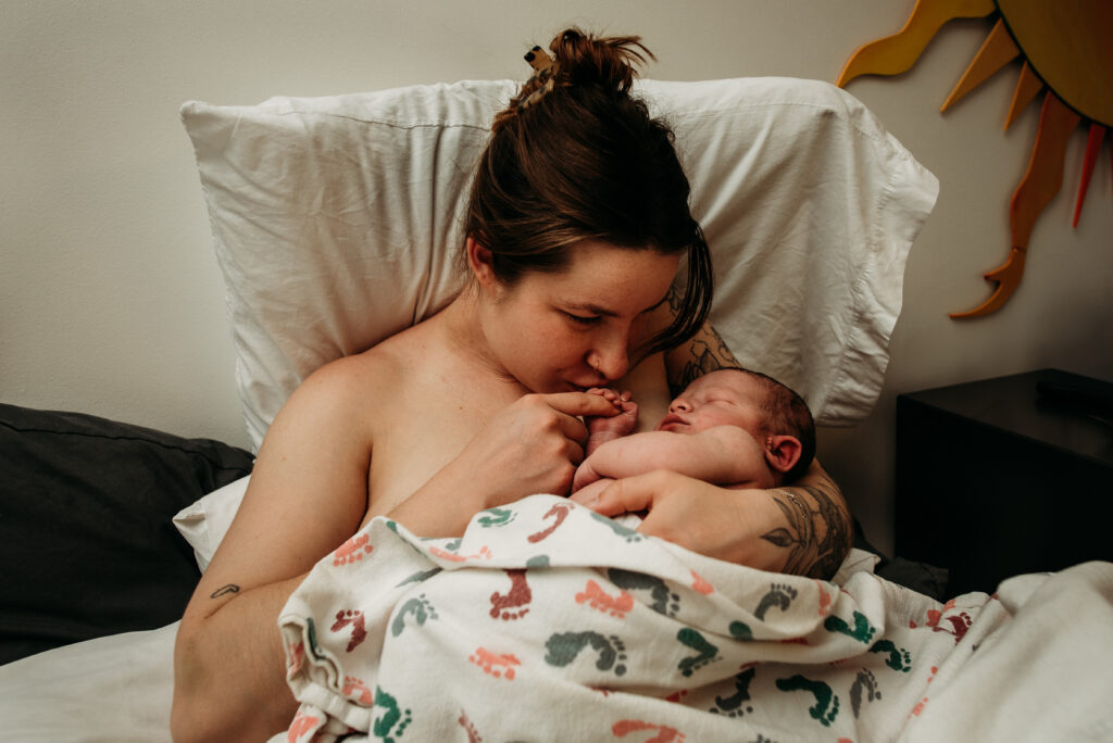 Mom kissing brand new baby's fingers in bed at birth center. Boulder Birth Holistic Health